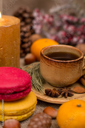 Cup of coffee, macaroons, cookies, walnuts, hazelnuts, cinnamon sticks, star anise, cone, candle, fir branch on sackcloth fabric