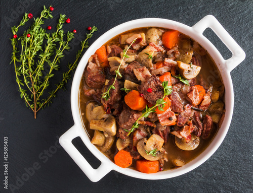 Beef Bourguignon in a casserole on black stone. Stewed with bacon, garlic, carrots, onions, mushrooms,  red wine, fresh thyme and spices. Top view. photo