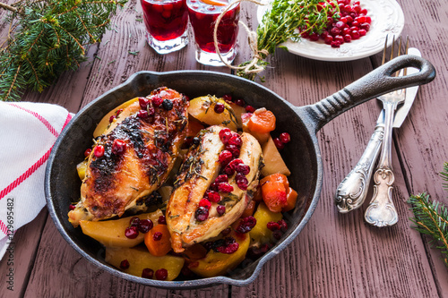 Baked chicken breast with carrots, cranberries and potatoes. Marinated with thyme, garlic and olive oil. Black cast-iron pan, wooden table.
