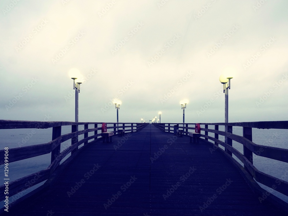 Pier at misty night with yellow lights on a background of dark blue sky