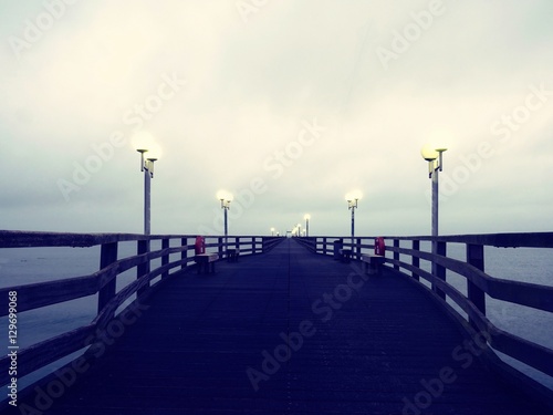 Pier at misty night with yellow lights on a background of dark blue sky