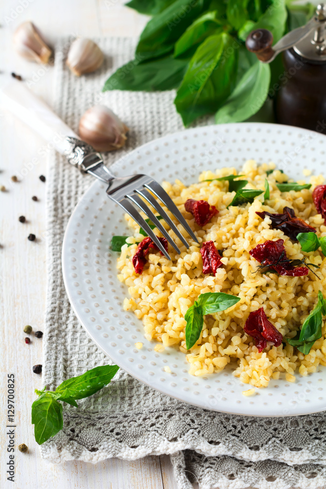 Bulgur with dried tomatoes and basil on a light wooden background. Vegetarian dish. Selective focus. Bulgur with dried tomatoes and basil on a light wooden background. Vegetarian dish. Selective focus.