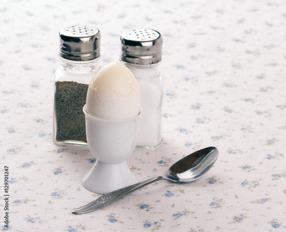 Egg in an egg cup, with spoon, salt and pepper shakers on an old fashioned table cloth Egg in an egg cup, with spoon, salt and pepper shakers on an old fashioned table cloth