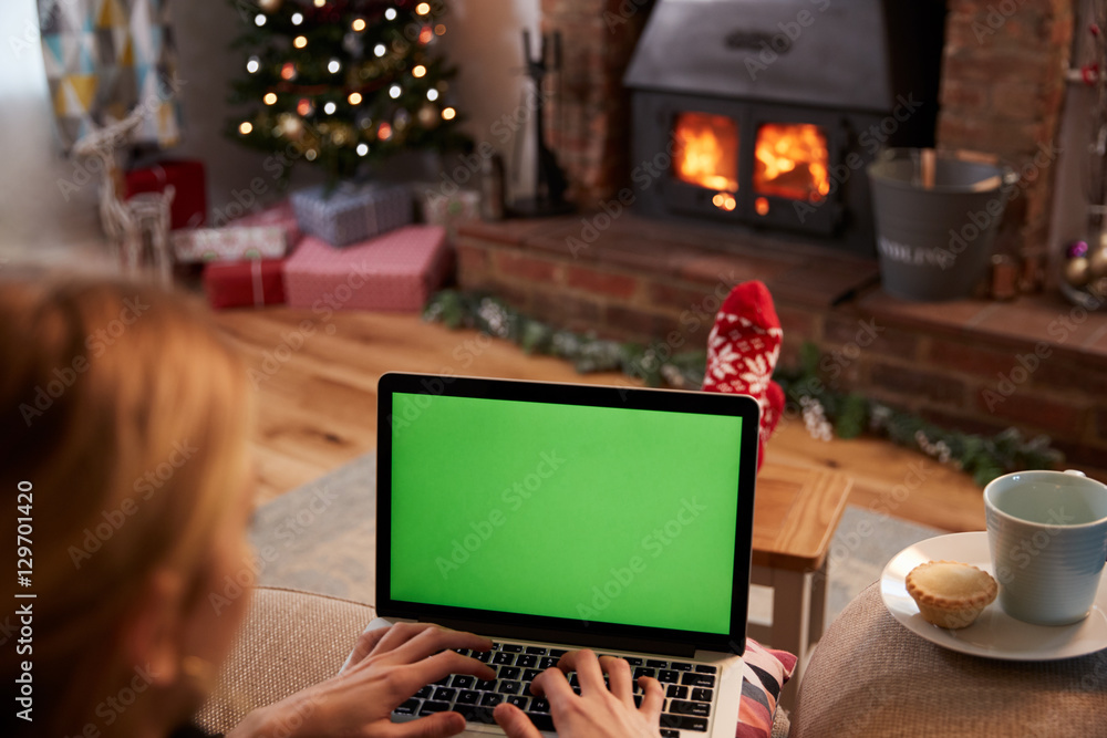 Woman Using Laptop In Room Decorated For Christmas Woman Using Laptop In Room Decorated For Christmas