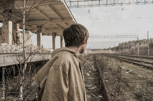 young boy goes rails near the abandoned train station. wandering boy. man in a protective cloak with a hood. Post apocalypse. traveling on foot in a post-apocalyptic world.