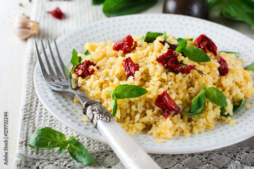 Bulgur with dried tomatoes and basil on a light wooden background. Vegetarian dish. Selective focus.