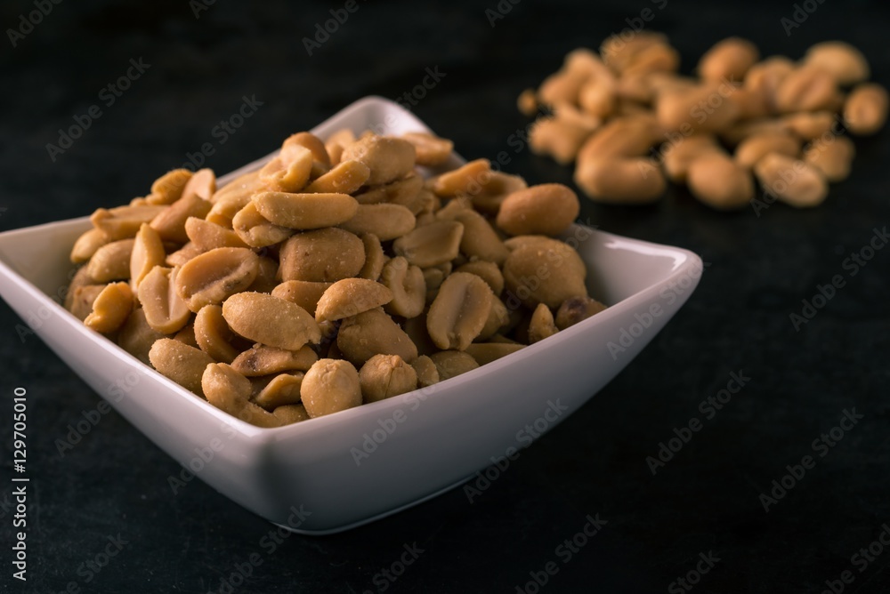 Peanuts in white bowl on dark tray Peanuts in white bowl on dark tray
