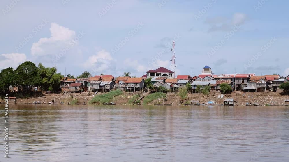 Village stilt-houses on the riverside at low tide under cloudy blue sky (shot from a moving boat) Village stilt-houses on the riverside at low tide under cloudy blue sky (shot from a moving boat)