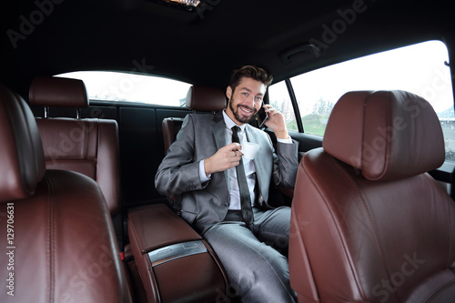 Happy young businessman using mobile phone in back seat of car