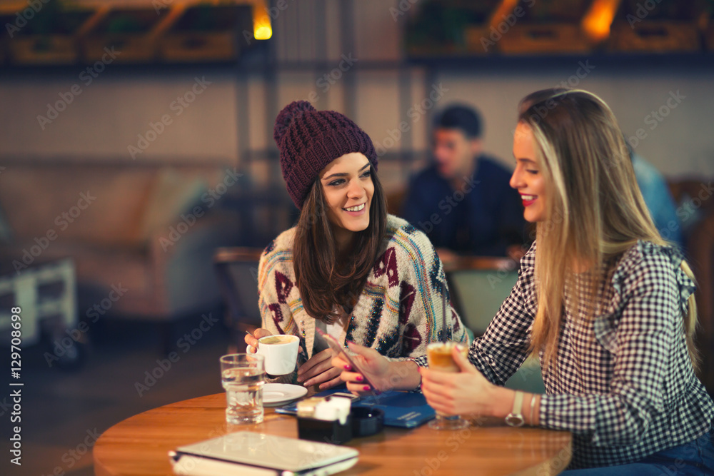 Fototapeta premium Two friends enjoying coffee together in a coffee shop as they si