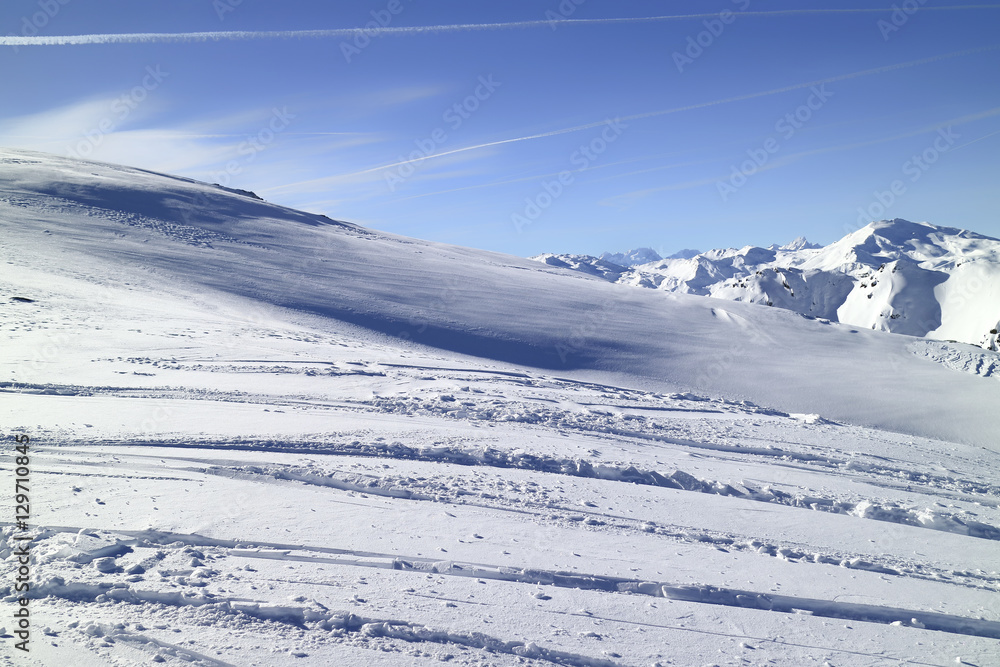 Winter landscape in high Alps with shimmering fresh snow, rugged peaks in the distance. Blue sky  with contrails.