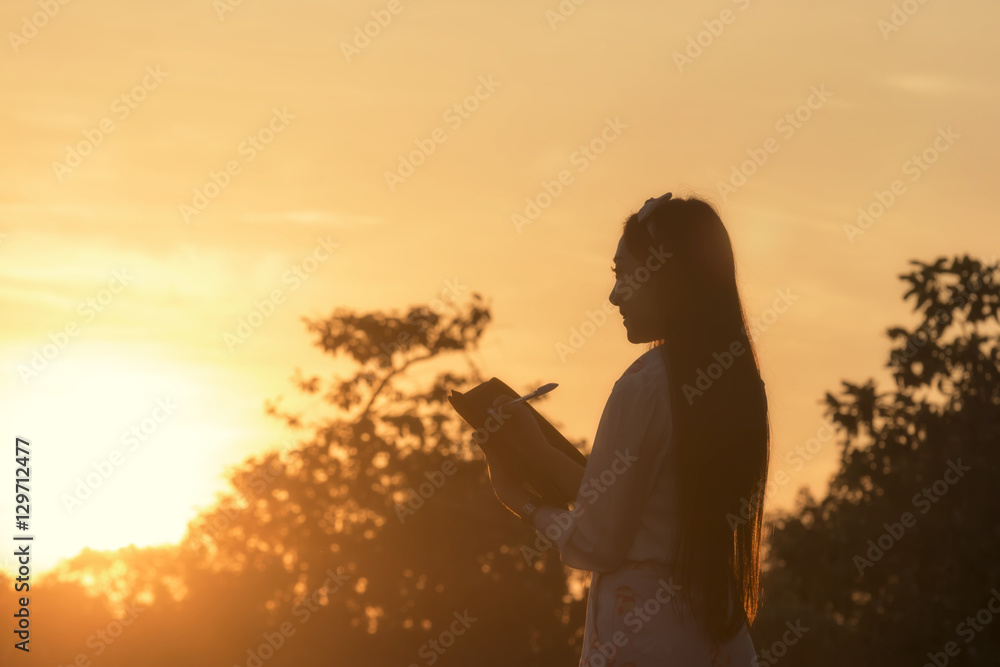 Young woman reading a book at meadow in summer sunset light.