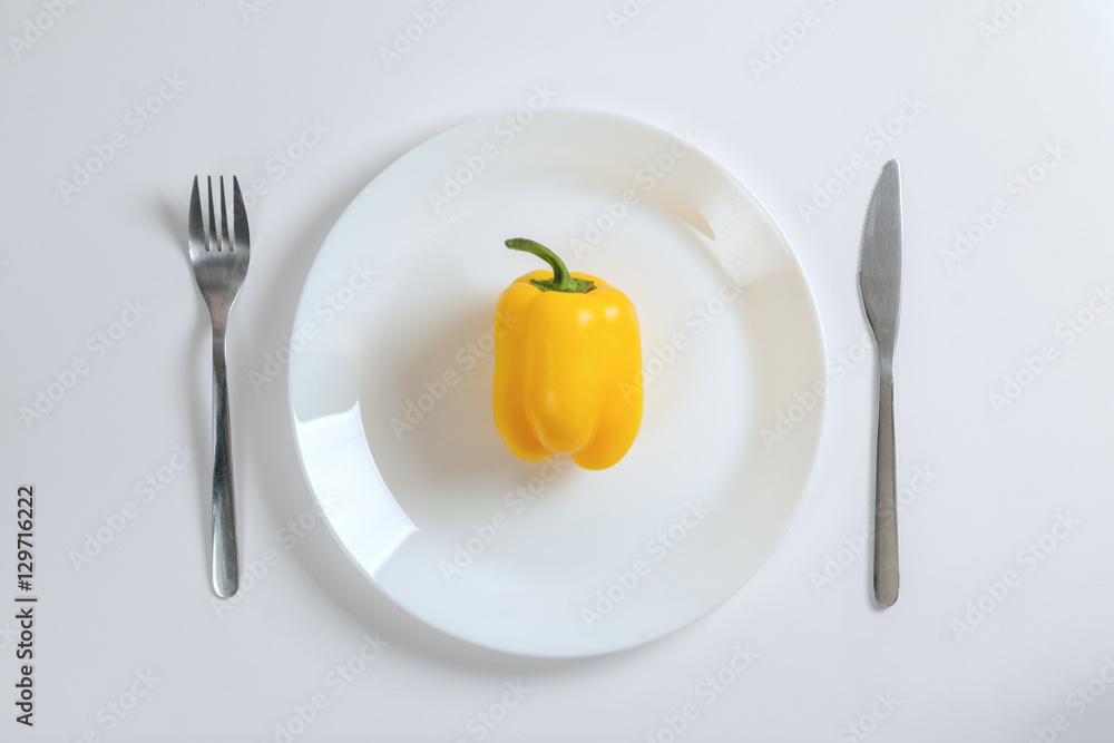 Knife, fork and yellow pepper, paprica on a white plate on a white background, top view Knife, fork and yellow pepper, paprica on a white plate on a white background, top view