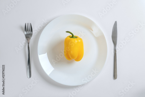Knife, fork and yellow pepper, paprica on a white plate on a white background, top view