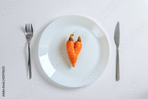 Knife, fork and carrot in a heart shape on a white plate on a white background, top view
