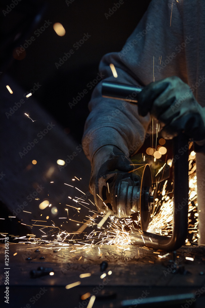 Man cutting steel pipe with many sharp sparks on a metal surface. Vertical photo.