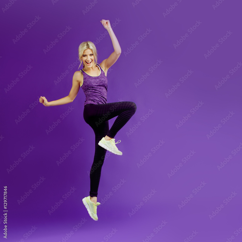 Beautiful young girl in a pose runner. Studio background, purple. Happy jumping