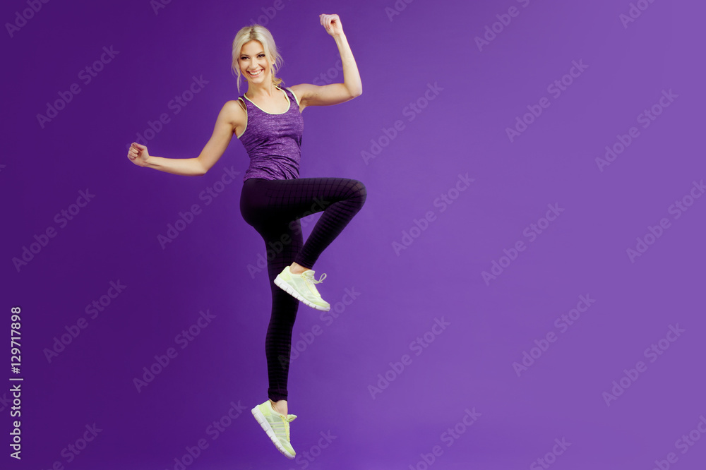 Beautiful young girl in a pose runner. Studio background, purple. Happy jumping