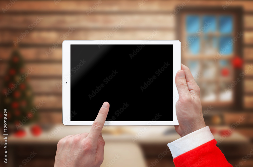 Tablet in Santa Claus hand with blank screen for mockup. Santa Claus home with Christmas tree in background.