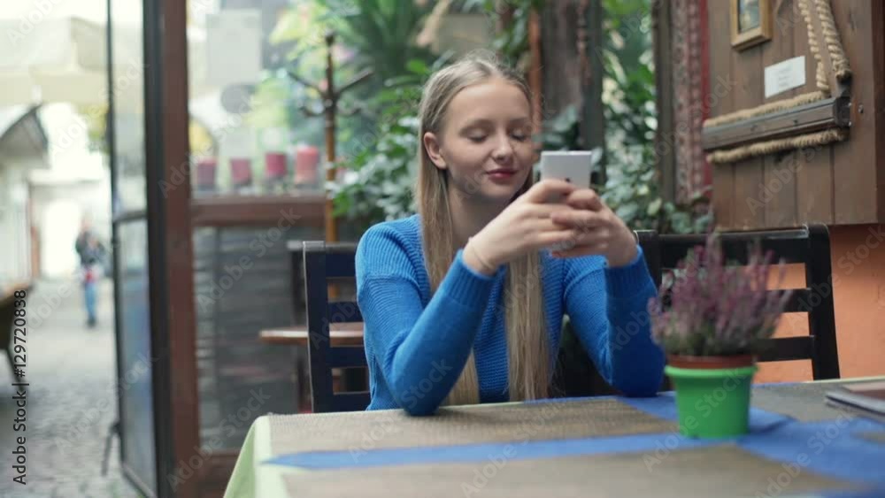 Girl texting on smartphone and smiling to the camera in the cafe
Girl texting on smartphone and smiling to the camera in the cafe