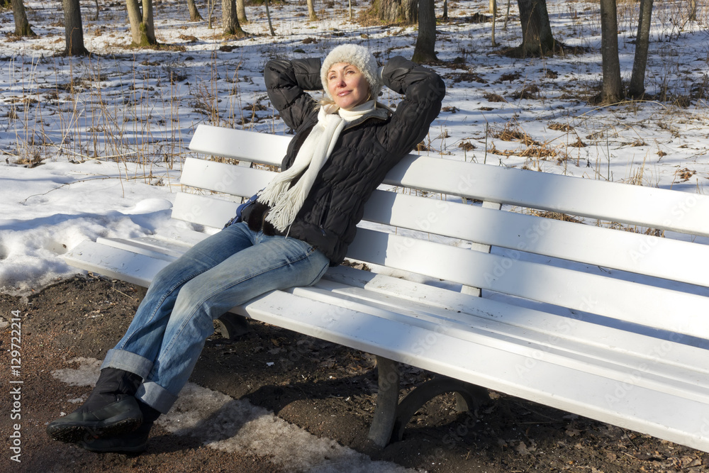 Fototapeta premium The young beautiful woman has a rest on a bench in the winter park..