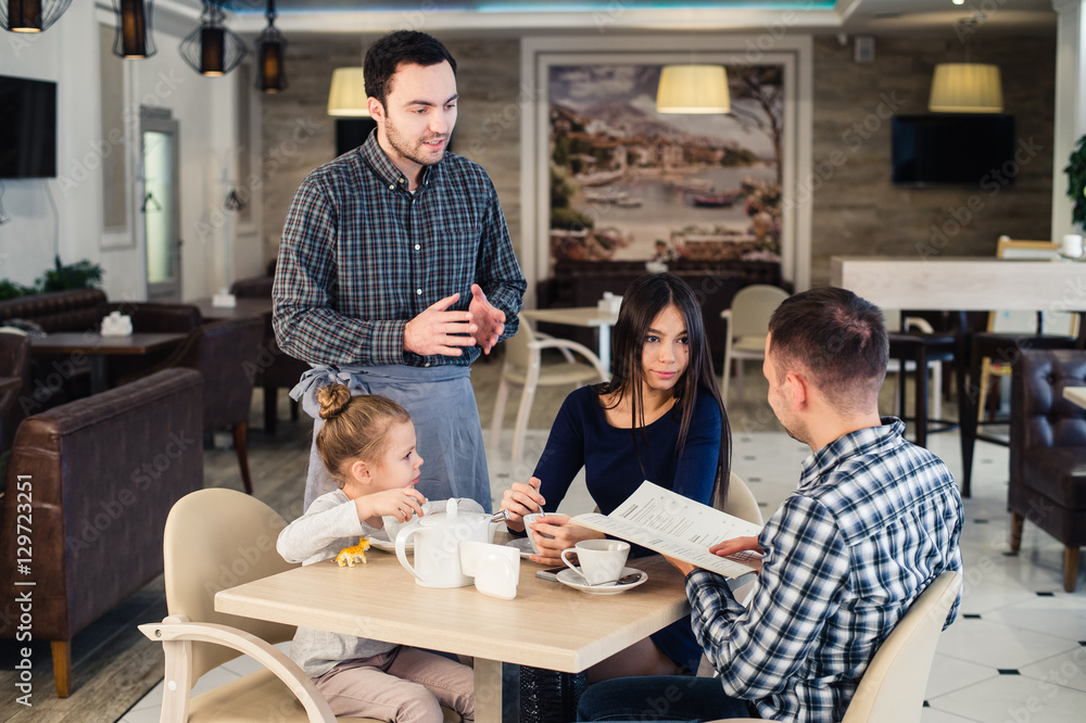 restaurant and holiday concept - waiter giving menu to happy family at cafe restaurant and holiday concept - waiter giving menu to happy family at cafe