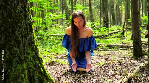 A woman in a blue dress found a big mushroom among wild forest. mystical mood.