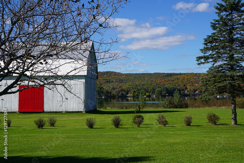 Gray barn with bright red door and green grass next to a lake in Mandeville, Quebec, Canada photo