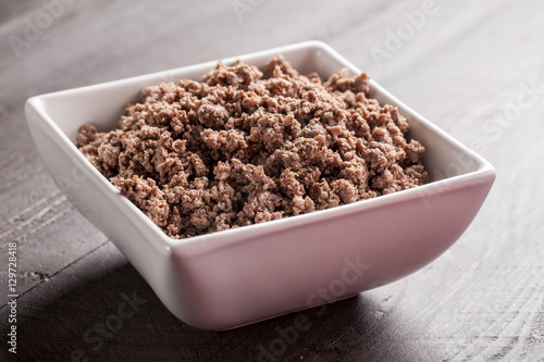 Small white bowl of cooked ground meat on brown wooden table