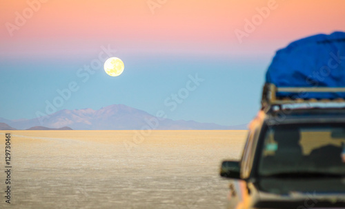 Full moon sunset with off road jeep vehicle on Salar De Uyuni - World famous nature wonder place in Bolivia - Travel and wanderlust concept in South American exclusive destination - Focus on infinity