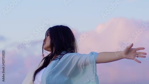 relaxing young woman opens arms to the sky suggestive clouds in background photo