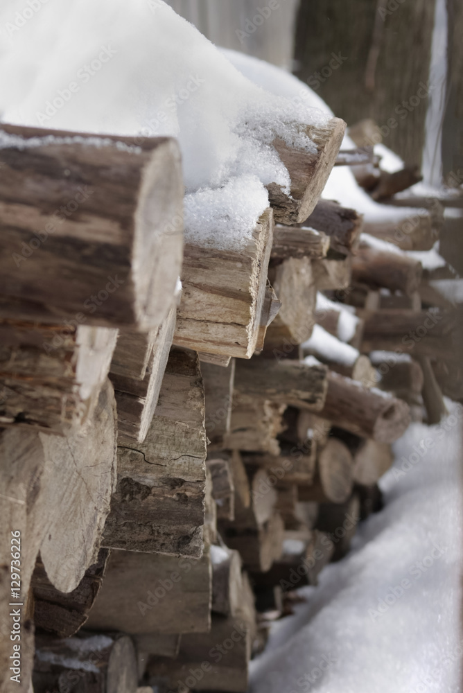 Stacked firewood logs covered in snow - cold winter day