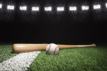 Baseball and bat at night under stadium lights on grass field