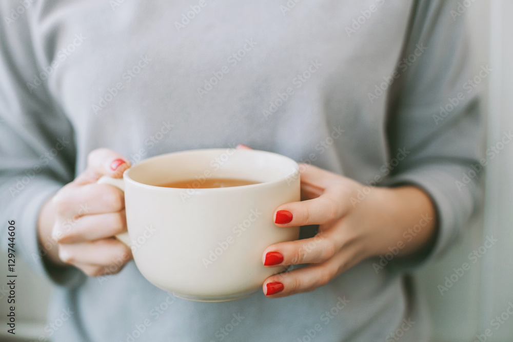 Young woman with bright red manicure and grey sweater holding a big white mug of tea with lemon Young woman with bright red manicure and grey sweater holding a big white mug of tea with lemon