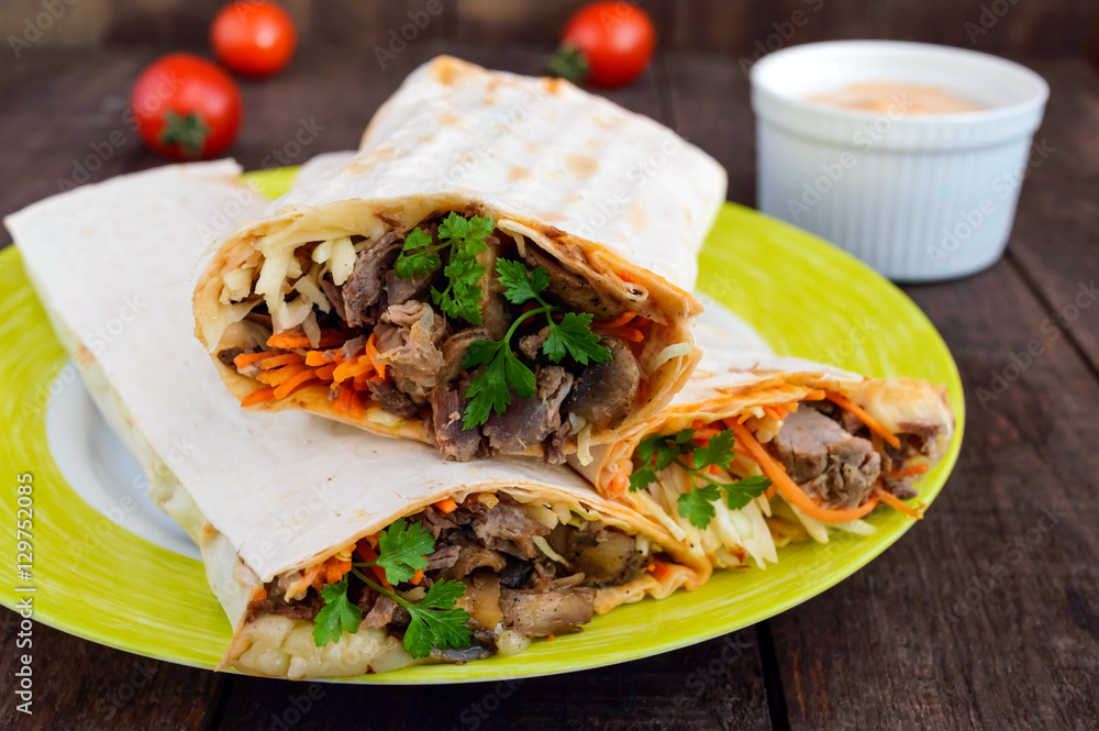 Shawarma sandwich - fresh roll of thin lavash (pita bread) filled with grilled meat, mushrooms, cheese, cabbage, carrots, sauce, green. Traditional Eastern snack. On a dark wooden background. Shawarma sandwich - fresh roll of thin lavash (pita bread) filled with grilled meat, mushrooms, cheese, cabbage, carrots, sauce, green. Traditional Eastern snack. On a dark wooden background.