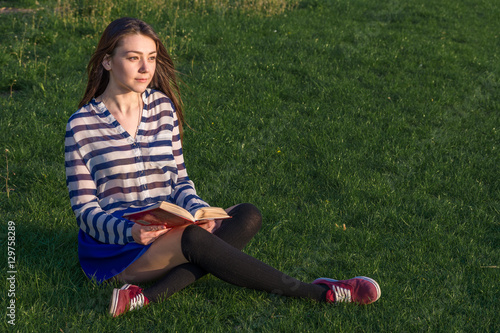 young woman reading a book in the park in spring