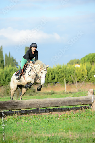 beautiful young woman riding horse and training for jump hurdle equitation competition outdoor