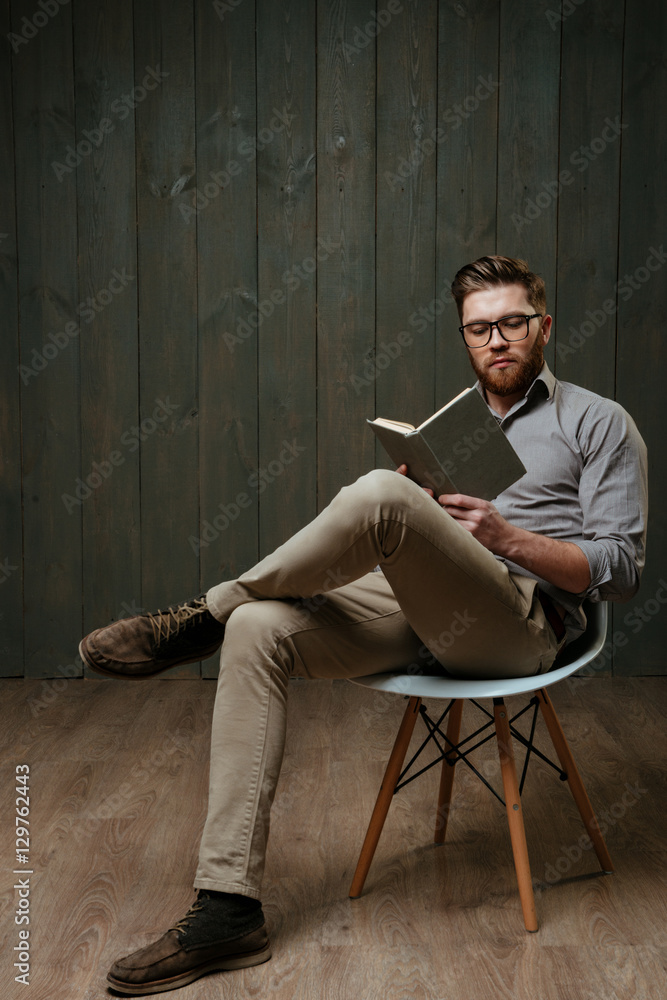 Young bearded man in eyeglasses sitting and reading a book Young bearded man in eyeglasses sitting and reading a book