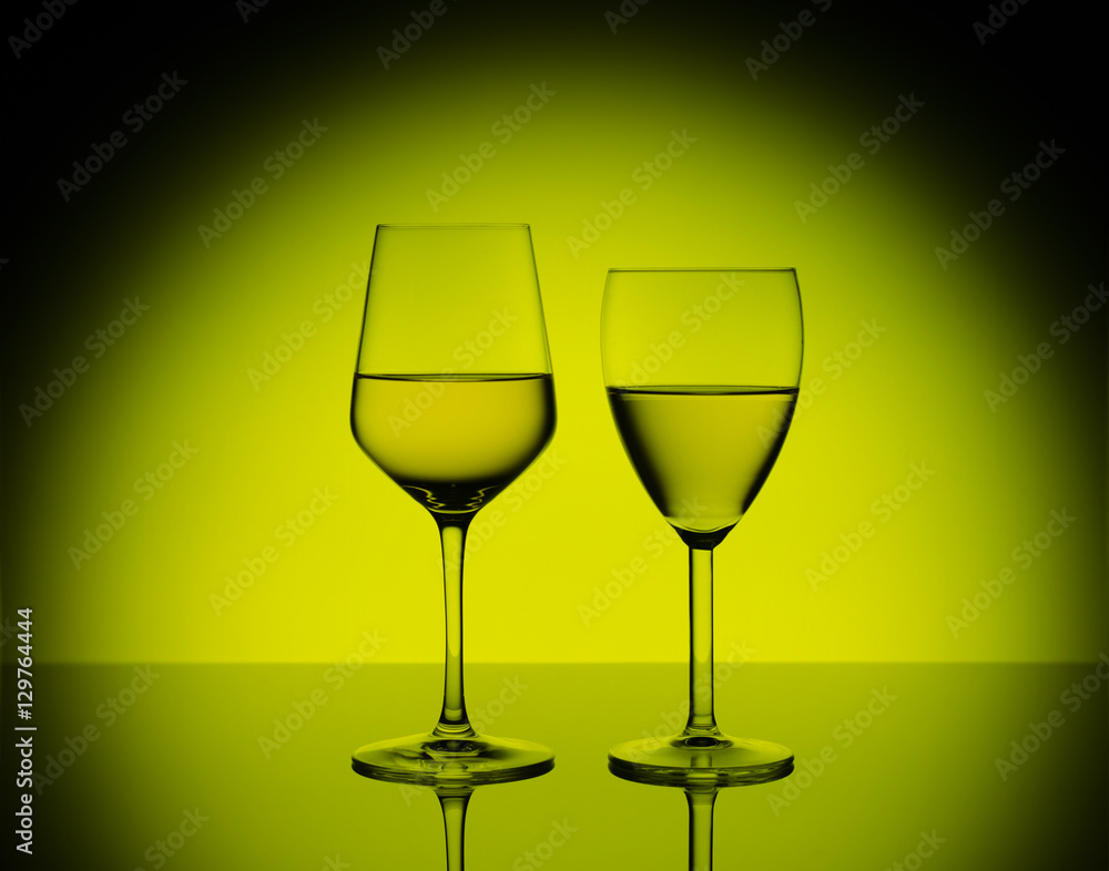 Two wineglasses with white wine on blurred yellow background