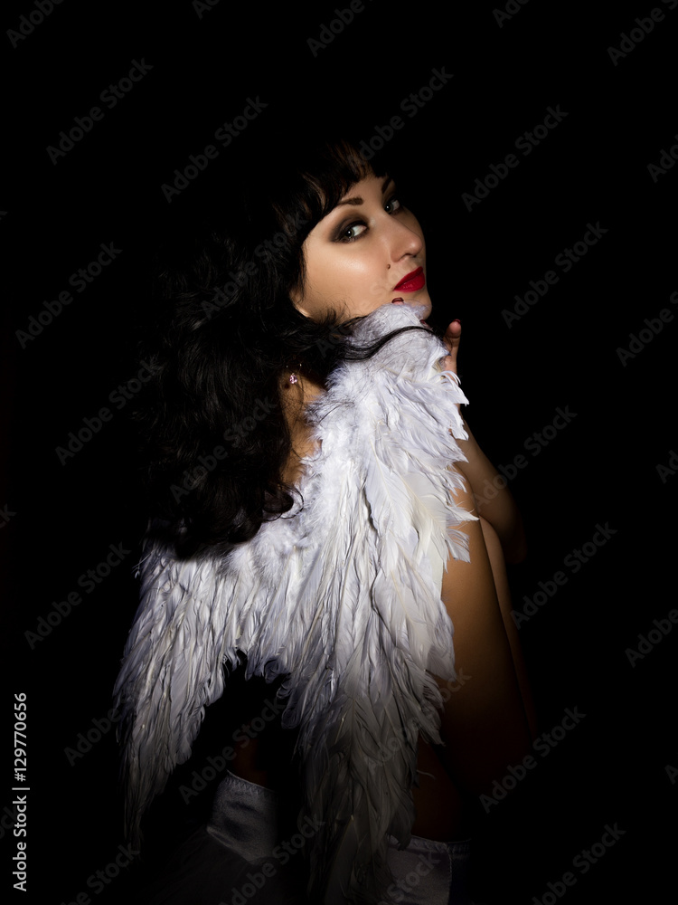 Beautiful bride wearing white dress with professional make-up and hairstyle, wings behind. on a dark background Beautiful bride wearing white dress with professional make-up and hairstyle, wings behind. on a dark background