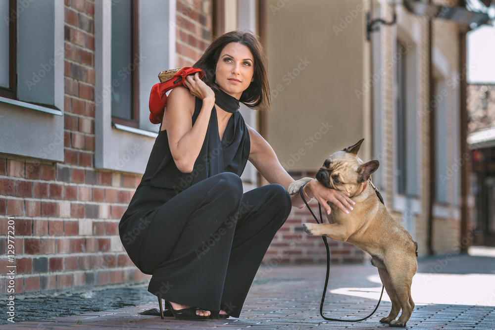 Obraz premium Beautiful young woman in black costume with cute small dog puppy posing on the street