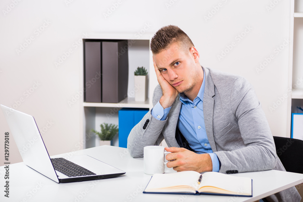 Exhausted businessman drinking coffee at his office.
Exhausted businessman drinking coffee at his office.