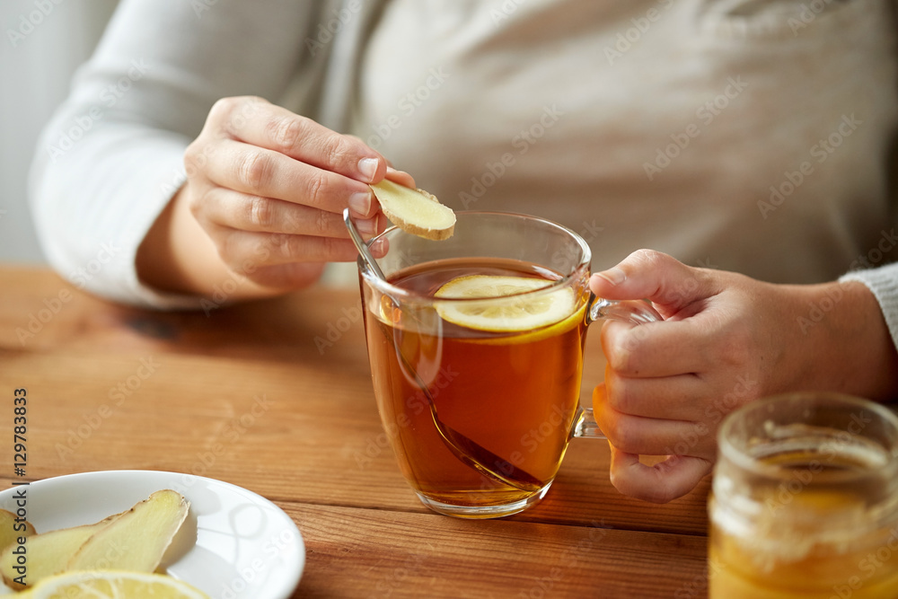 close up of woman adding ginger to tea with lemon close up of woman adding ginger to tea with lemon