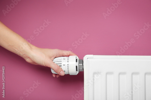 Fotografie Female hand on temperature regulator of heating battery on pink background, clos
