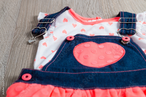 Coral and blue dress, overalls with heart on grey wooden background. Little girl outfit. Close up.