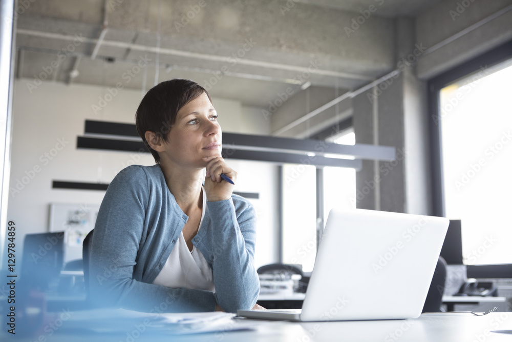 Businesswoman in office with laptop thinking Businesswoman in office with laptop thinking