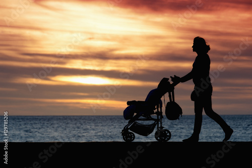 Silhouette mother pulling baby stroller against beach sunset