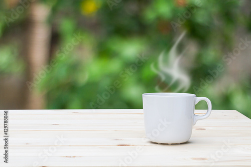 Hot coffee with steam on wooden table top on blurred garden background