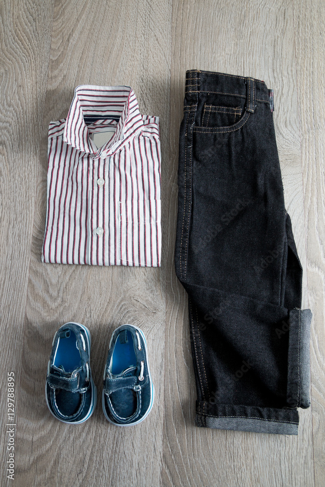 Boy outfit. Striped shirt, denim pants and blue shoes on grey wooden background.. Top view. Boy outfit. Striped shirt, denim pants and blue shoes on grey wooden background.. Top view.