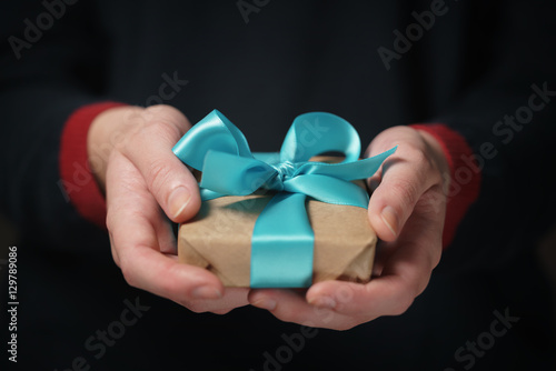 female teen hands show craft paper gift box with blue bow, shallow focus
